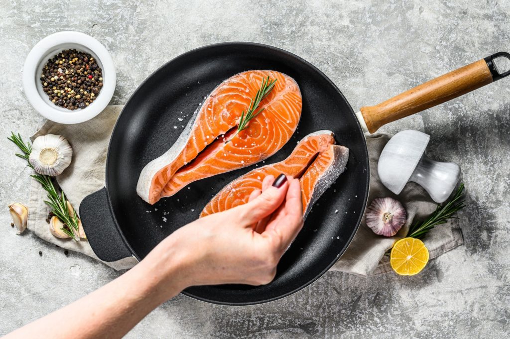 Chef salts raw salmon steak in a frying pan. Healthy seafood