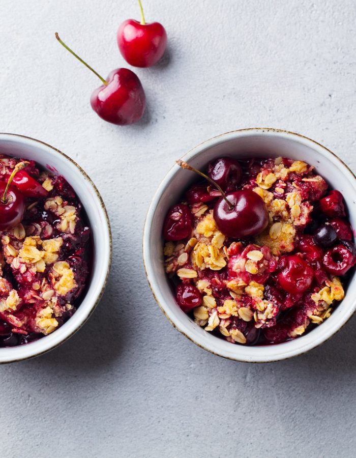 Cherry, red berry crumble in bowl. Grey stone background. Top view.